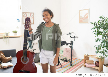 Happy schoolgirl with guitar standing in the center of domestic room Happy schoolgirl with guitar standing in the center of domestic room 83348783