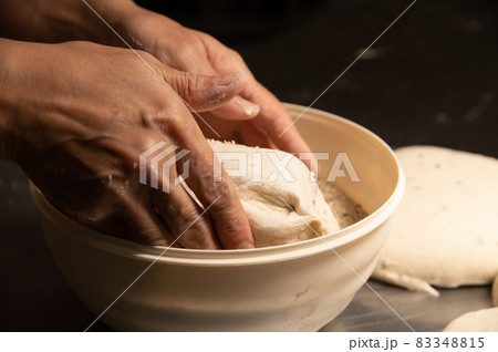 close-up of a baker's female hands dipping dough into a bowl of seeds and cereals before baking artisan bread at a home bakery close-up of a baker's female hands dipping dough into a bowl of seeds and cereals before baking artisan bread at a home bakery 83348815
