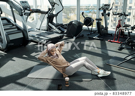 Young pretty sportswoman doing sit-ups with side turns Young pretty sportswoman doing sit-ups with side turns 83348977