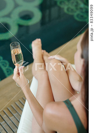 Young woman holding flute of champagne while sitting by poolside Young woman holding flute of champagne while sitting by poolside 83349099