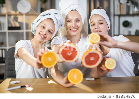 Two sisters with mother using slices of citrus for skin care 83354876
