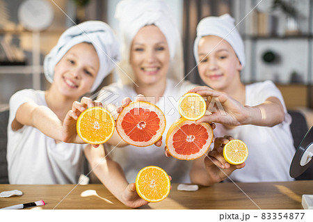 Woman with two daughters holding slices of citrus at table 83354877