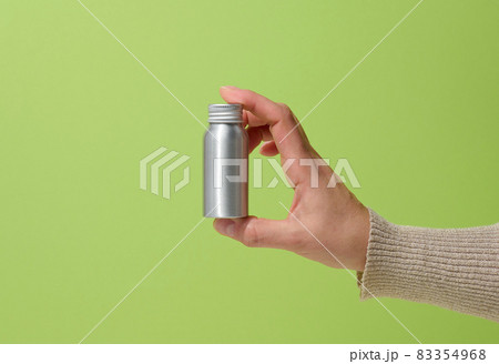 female hand holding a silver metal bottle for cosmetics on a green background 83354968