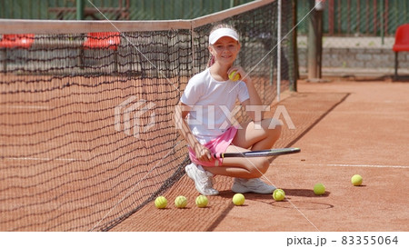 Girl tennis player sits on the court and throws balls. Girl tennis player sits on the court and throws balls. 83355064