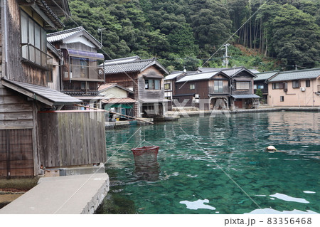大きな石の海底が見える透明度の高いエメラルド色の海と網と舟屋と山の風景 83356468