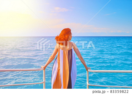 Cute girl in flowing long dress stands on edge of sea pier. Cute girl in flowing long dress stands on edge of sea pier. 83359822