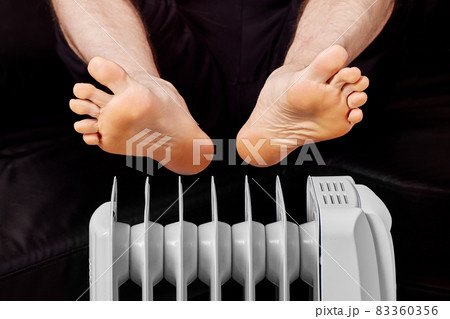 Electric oil heater with man who warms his feet. Electric oil heater with man who warms his feet. 83360356
