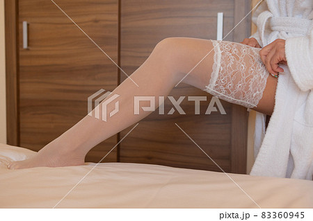 Unrecognizable bride in a silk robe with beautiful slim legs is putting on stockings. Wedding morning preparation. Dressing lingerie, boudoir. 83360945