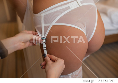 Unrecognizable bride in a silk robe with beautiful slim legs is putting on stockings. Wedding morning preparation. Dressing lingerie, boudoir. 83361341