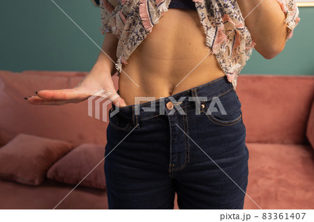 Weight Loss and Body Image Concept. Young Woman Shows her Weight Loss and Wearing Her Old Jeans. Slim Girl in Big Jeans Showing How She Was Losing Weight When She Started Eating Healthy Food. 83361407