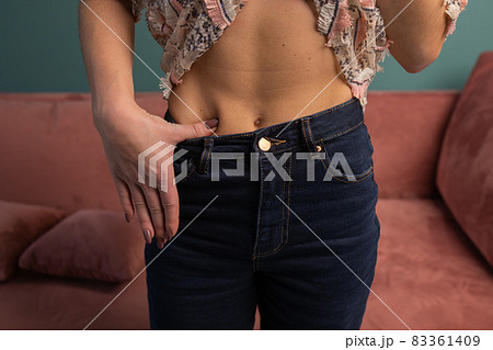 Weight Loss and Body Image Concept. Young Woman Shows her Weight Loss and Wearing Her Old Jeans. Slim Girl in Big Jeans Showing How She Was Losing Weight When She Started Eating Healthy Food. 83361409