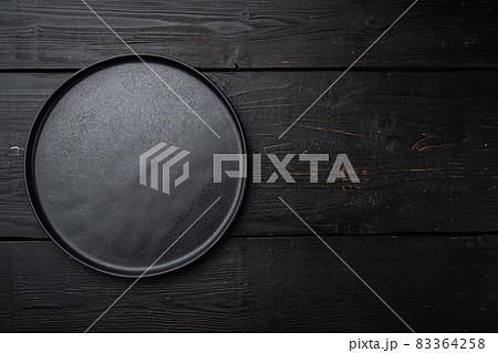 Empty black plate, on black wooden table background Empty black plate, on black wooden table background 83364258
