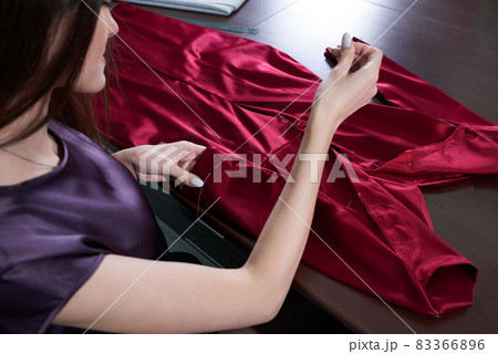 Beautiful young dressmaker in workroom sewing red dress in tailor studio or atelier shop Beautiful young dressmaker in workroom sewing red dress in tailor studio or atelier shop 83366896