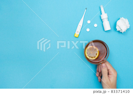 Man holding a cup of tea with lemon. Flu season. Pills, nasal spray, used wipes, and thermometer. Catch a cold. Disease. Flat lay. Seasonal cold concept. Place for your text. Copy space. Mockup. 83371410