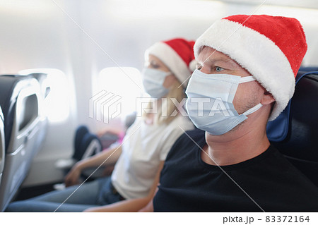 Man and woman in santa hats and protective face masks flying in airplane Man and woman in santa hats and protective face masks flying in airplane 83372164