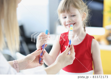 Dentist doctor holding two toothbrushes in front of little girl closeup Dentist doctor holding two toothbrushes in front of little girl closeup 83372173