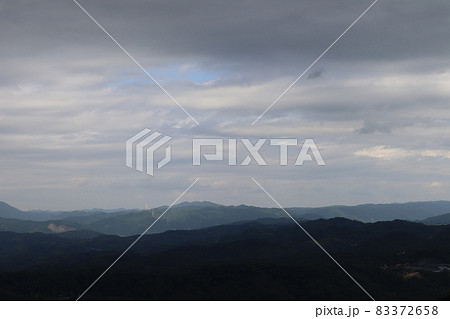 雲の厚い暗い空と少しの青空と近くは暗く遠くは明るい連なる山々の見える風景 83372658