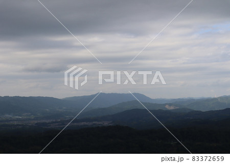 雲の厚い暗い空と連なる山々と谷間にある町の見える風景 83372659