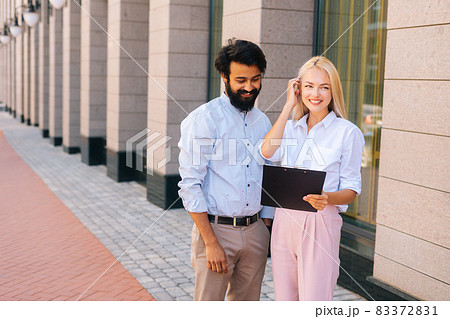 Medium shot portrait of cheerful male and female colleagues discussing document on clipboard standing in city street by office building. Medium shot portrait of cheerful male and female colleagues discussing document on clipboard standing in city street by office building. 83372831