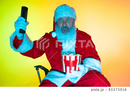 Portrait of senior man, surprised Santa Claus sitting and watching movie at cinema, indoors. Happy New Year 2022, Christmas concept 83373916