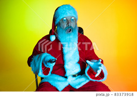 Portrait of senior man, surprised Santa Claus sitting and watching movie at cinema, indoors. Happy New Year 2022, Christmas concept 83373918