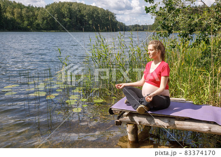 Pregnant woman doing yoga exercise meditating in a summer forest 83374170