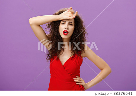 Woman fainting feeling bad whiping sweat of forehead standing drained and exhausted over purple background in red stylish dress expressing gloomy and unhappy feelings wanting some help Woman fainting feeling bad whiping sweat of forehead standing drained and exhausted over purple background in red stylish dress expressing gloomy and unhappy feelings wanting some help 83376641