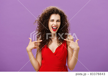 Woman celebrating successful sign of deal, pleased and satisfied bragging about own achievements pointing at herself smiling joyfully with triumph standing in evening red dress over purple background Woman celebrating successful sign of deal, pleased and satisfied bragging about own achievements pointing at herself smiling joyfully with triumph standing in evening red dress over purple background 83376643