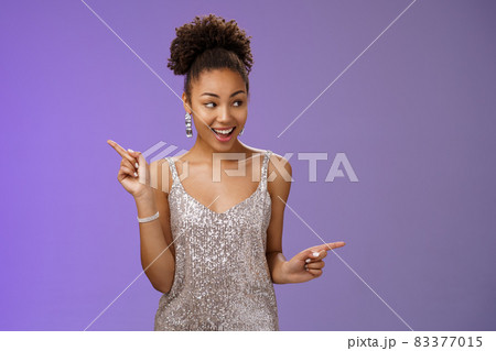 Good-looking excited glamour african-american female student attend luxurious event in silver shiny perfect dress dancing look around pointing right left smiling pleased variants make choice 83377015