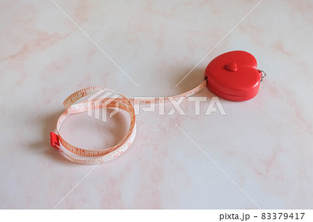 Tape measure in the heart shape on the pink marble background. Tape measure in the heart shape on the pink marble background. 83379417