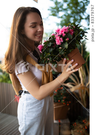 happy caucasian young woman chooses potted flowers to buy at outdoor garden stall 83379767