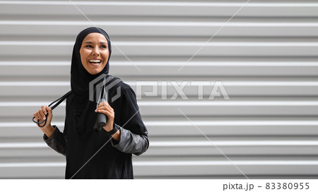 Cheerful Young Muslim Woman In Modest Sportswear Posing With Skipping Rope Outdoors Cheerful Young Muslim Woman In Modest Sportswear Posing With Skipping Rope Outdoors 83380955