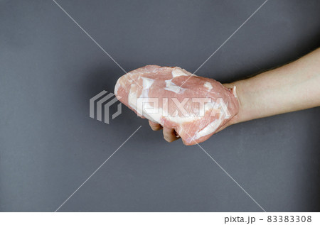 The hand holds the raw pork meat on the gray. A grown man and a 83383308