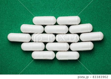 white capsules pills on green background 83383902