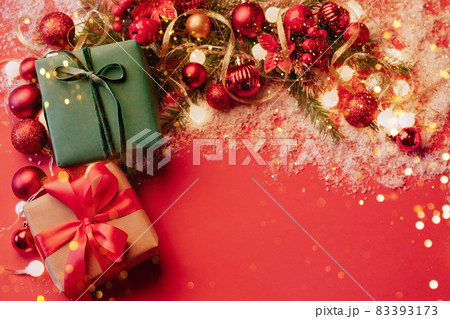 Festive boxes on a red background with Christmas toys balls a branch of fluffy fir tree, sparkles with confetti lights. New Year Christmas concept. Flat festive mockup with copy space 83393173