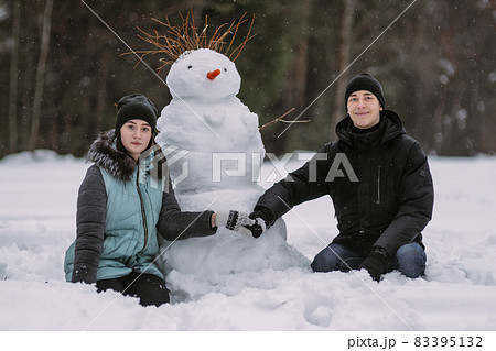 Couple of teenagers building snowman together in winter Couple of teenagers building snowman together in winter 83395132