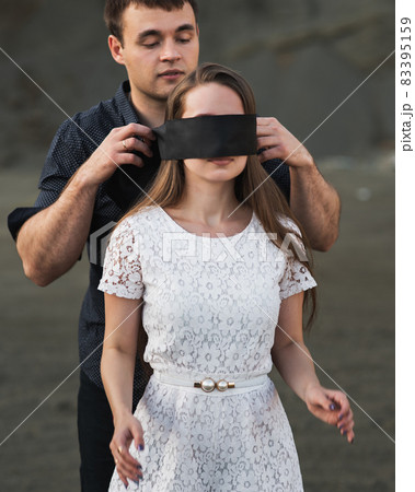 Romantic man blindfolding his woman with black ribbon. Love blind concept 83395159