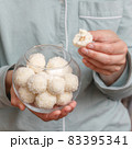 Coconut candy balls in glass bowl in hands of woman 83395341