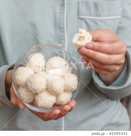 Coconut candy balls in glass bowl in hands of woman 83395341