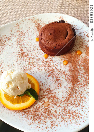 Close up of hot melting chocolate cake dessert and scoop of vanilla ice cream on orange slice on white plate. Chocolate fondant and ice cream. Top view, vertical photo. Close up of hot melting chocolate cake dessert and scoop of vanilla ice cream on orange slice on white plate. Chocolate fondant and ice cream. Top view, vertical photo. 83395921