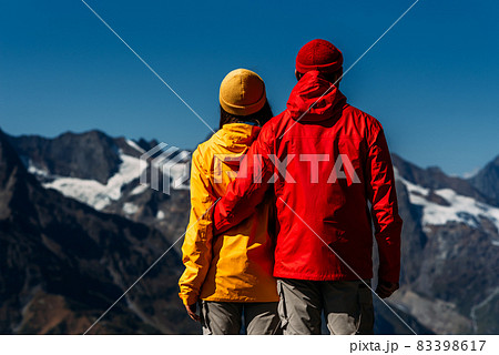People in colorful jackets on the background of the mountains, rear view. An active couple is engaged in Hiking. A young couple is engaged in tracking. Hiking. People in the mountains 83398617