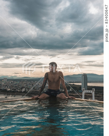 The view from the hotel rooftop pool of the city and the guy sitting on the edge of the rooftop swimming pool. Picturesque view, beautiful sky  83400647
