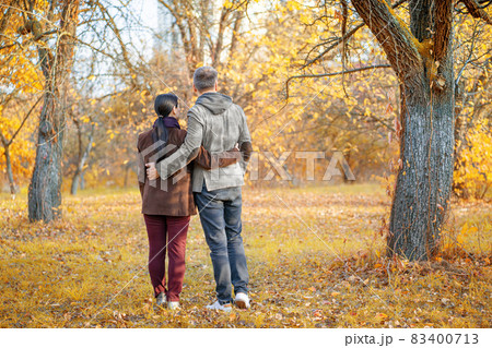 Nice Pair Admires the Amazing Fall Nature Around. Couple Enjoying One Another And the Good Weather Outside. Standing Back to Camera. Autumn Background. Full-length Nice Pair Admires the Amazing Fall Nature Around. Couple Enjoying One Another And the Good Weather Outside. Standing Back to Camera. Autumn Background. Full-length 83400713