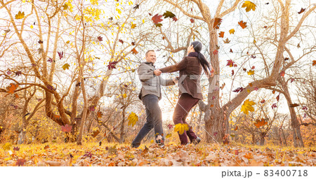 A Man and a Woman Whirling Together Holding Hands and Enjoy Sunny Autumn Weather in the Park. Two Lovers Look at One Another in Fall Forest. Autumn Background. Full-length  83400718