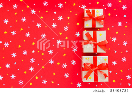 Three beautiful gifts are decorated with a ribbon. On a red background with gold and silver stars and snowflakes. Postcard for Christmas and New Year. Three beautiful gifts are decorated with a ribbon. On a red background with gold and silver stars and snowflakes. Postcard for Christmas and New Year. 83403785