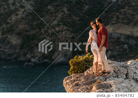 A man embraces a beautiful woman on the edge of a cliff by the sea. A couple in love at sunset. Beautiful couple meets sunset by the sea. Happy couple having fun on the coast. Copy space 83404782