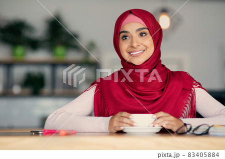 Relaxed middle eastern woman in hijab enjoying coffee at cafe 83405884