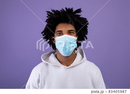 Black teenager wearing medical protective mask during coronavirus pandemic on violet studio background 83405987