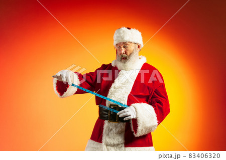 Emotional senior man, Santa Claus posing isolated on red yellow background in neon. Healthy New Year 2022 83406320