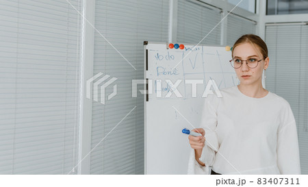 Young business woman, speaker coach drawing on white board and having online meeting in office. Focused team leader businesswoman, project manager working with white board Young business woman, speaker coach drawing on white board and having online meeting in office. Focused team leader businesswoman, project manager working with white board 83407311